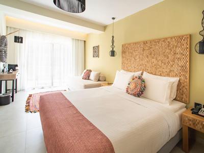 Licht hotelkamer met groot bed en balkon met witte gordijnen.