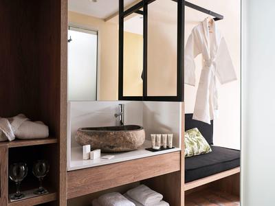 Modern hotelkamer met wasbak, badjas en gezellige zithoek met kussens.