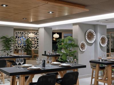 Ristorante moderno con tavoli apparecchiati, piante e accenti decorativi alle pareti.