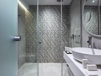Moderne badkamer met glazen douche, mozaïektegels en ronde spiegel.