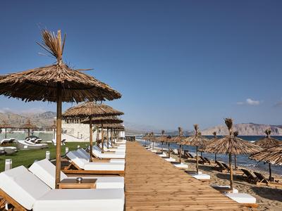 Zonnige strandpromenade met ligstoelen en rieten parasols onder een heldere lucht.