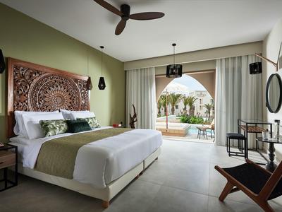 Lichte hotelkamer met groot bed, sierlijke wanddecoratie en uitzicht op een terras.