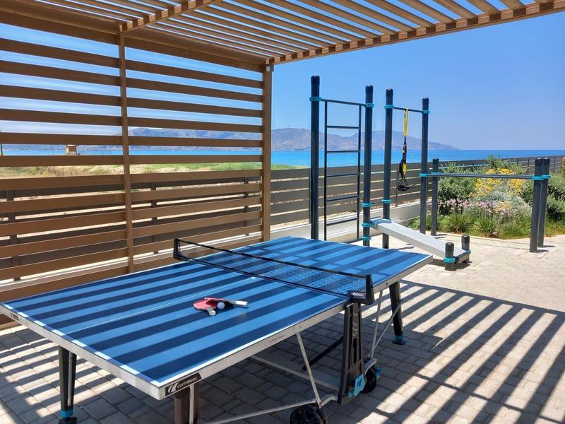 Zonterras met tafeltennistafel en zeezicht onder houten latten.