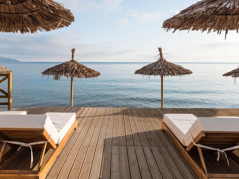 Houten terras met ligstoelen en strooien parasols aan de rustige zee.