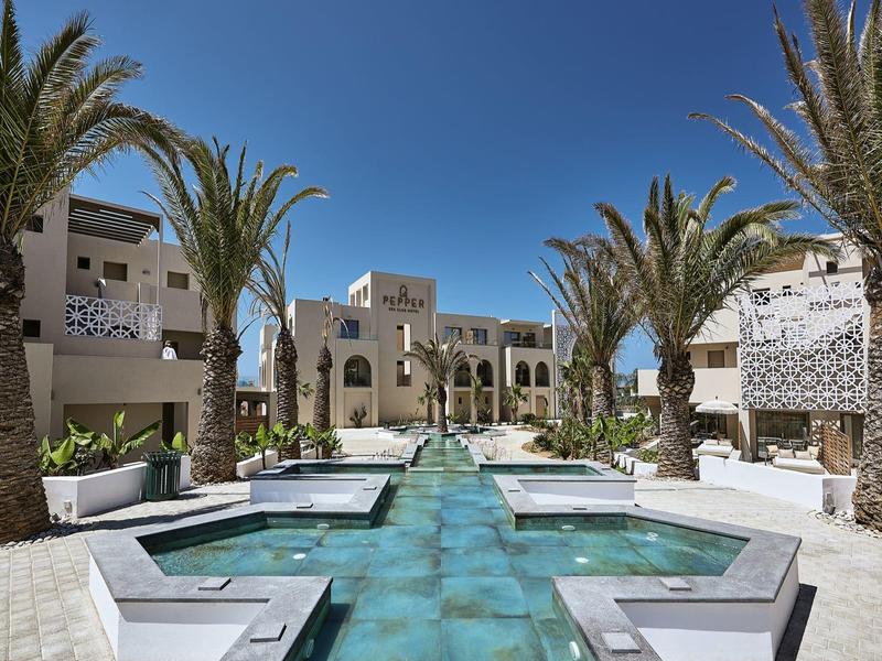 Luxe hotel met zwembad en palmbomen onder een heldere blauwe lucht.