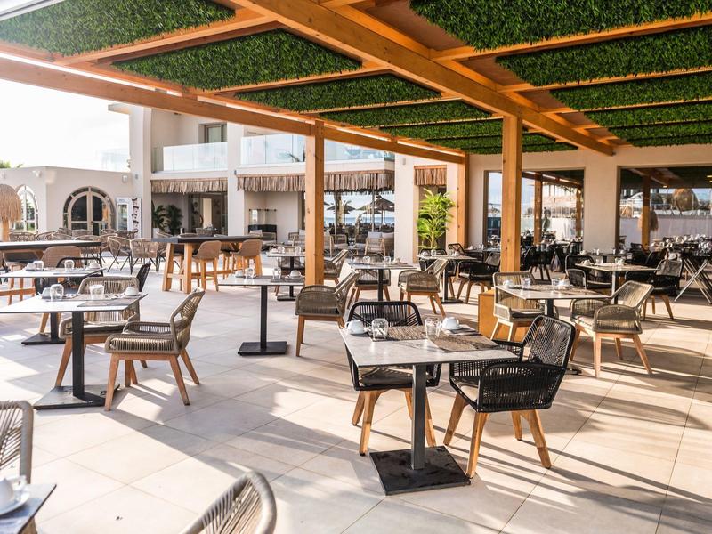 Zonnig buitenterras van een restaurant met tafels en stoelen onder een groen dak.