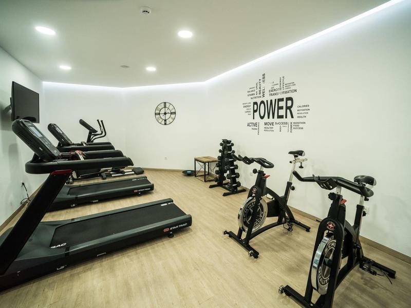 Lichte fitnessruimte met loopbanden, spinningfietsen en dumbbells.