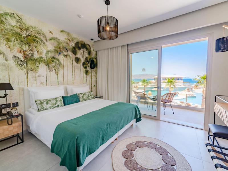 Lichte slaapkamer met groot bed, groene dekens en balkon met uitzicht op zee.