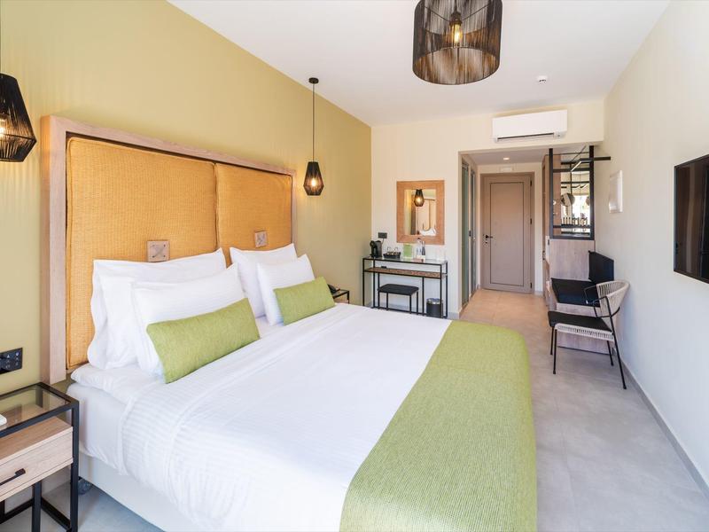 Moderne hotelkamer met groot bed, groene loper en stijlvolle lampen.