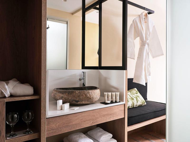 Modern hotelkamer met wasbak, badjas en gezellige zithoek met kussens.