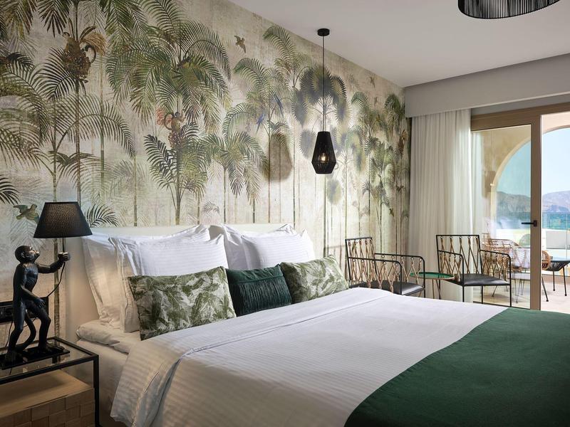 Modern slaapkamer met groot bed, tropisch behang en terras met uitzicht op zee.