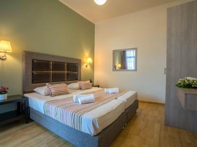 Nowoczesny pokój hotelowy z podwójnym łóżkiem, stolikami nocnymi i miękkim oświetleniem ściennym.