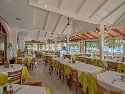 Duża otwarta restauracja z żółtymi obrusami i drewnianymi meblami, otoczona naturą.