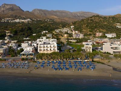 Plage avec parasols bleus et bâtiments blancs devant un paysage vallonné sous un ciel clair