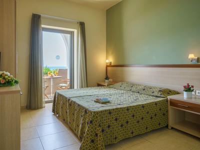 Acogedora habitación de hotel con cama doble, colcha verde con estampado y acceso al balcón.