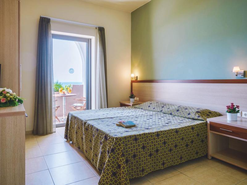 Chambre d'hôtel confortable avec lit double, mur vert et accès au balcon.