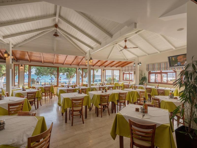 Restaurant lumineux avec de nombreuses tables dressées et des meubles en bois donnant sur une terrasse.
