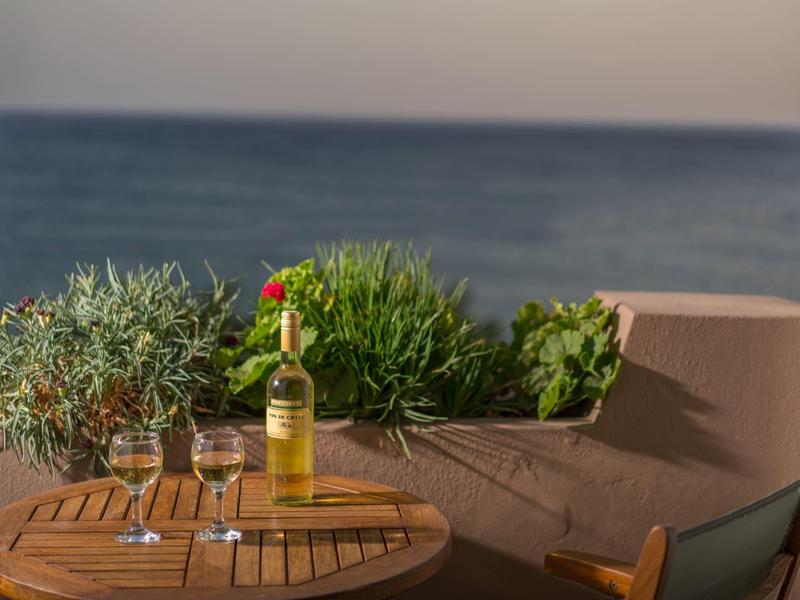Table sur balcon avec bouteille de vin, deux verres et vue sur la mer en arrière-plan.
