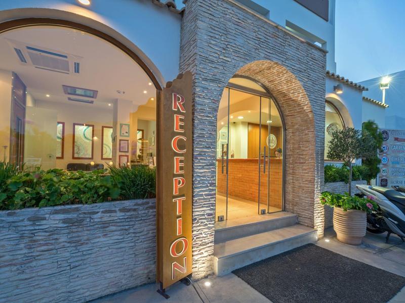 Entrée d'hôtel éclairée avec mur en pierre et porte de réception au crépuscule.