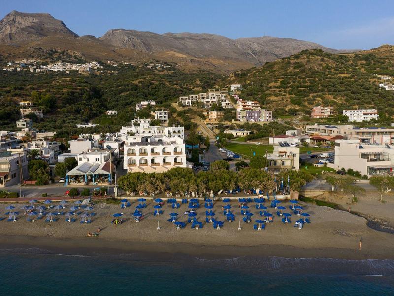 Plage avec parasols bleus et bâtiments blancs devant un paysage vallonné sous un ciel clair