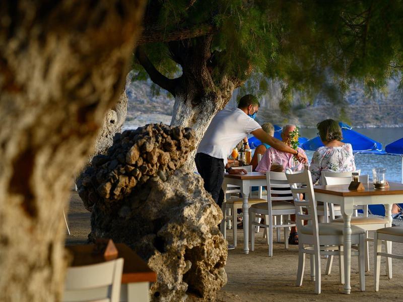 Un serveur sert des clients à une table en plein air sous des arbres.