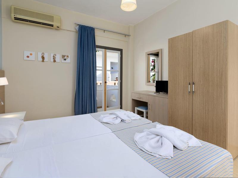 Chambre d'hôtel lumineuse avec deux lits, armoire, bureau et climatisation.