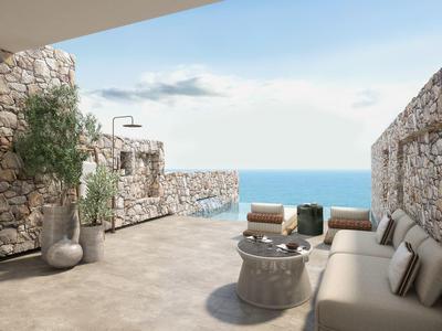 Terrasse mit Steinmauern, bequemen Sitzmöbeln und Blick auf das blaue Meer unter blauem Himmel.