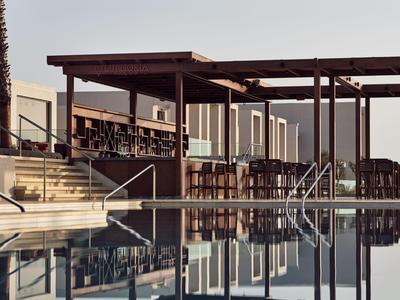 Moderner Poolbereich mit Holzüberdachung, Stühlen und Spiegelung im ruhigen Wasser.