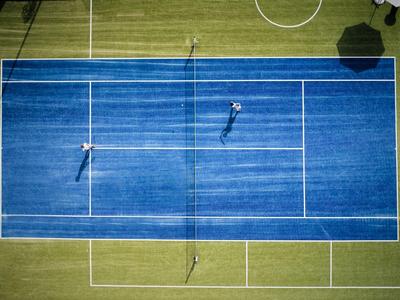 Luftaufnahme eines blauen Tennisplatzes mit zwei Spielern und grüner Umgebung.