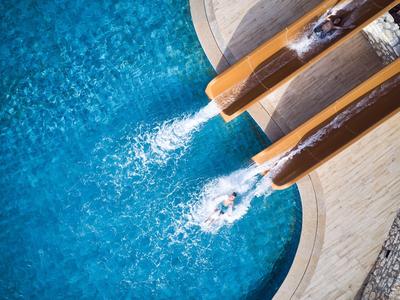 Blaues Wasser im Pool mit drei Wasserstrahlen aus braunen Rohren, umgeben von hellem Rand.