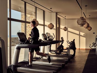 Frau läuft auf Laufband in hellem Fitnessraum mit großen Fenstern und Blick auf Stadt.
