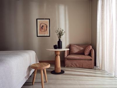 Minimalistisches Wohnzimmer mit braunem Sessel, Holzhockern, kleinem Tisch und gerahmtem Bild an der Wand.