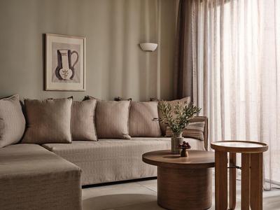 Gemütliche Sitzecke mit beige Couch, sechs Kissen, zwei runden Holztischen und grüner Pflanze.