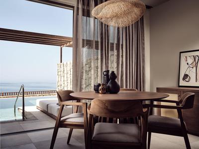 Moderner Essbereich mit rundem Holztisch und Stühlen, Blick auf Terrasse und Meer im Hintergrund.