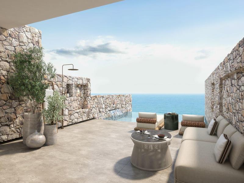 Open terrace with stone walls, beige sofa, and sea view under a blue sky.