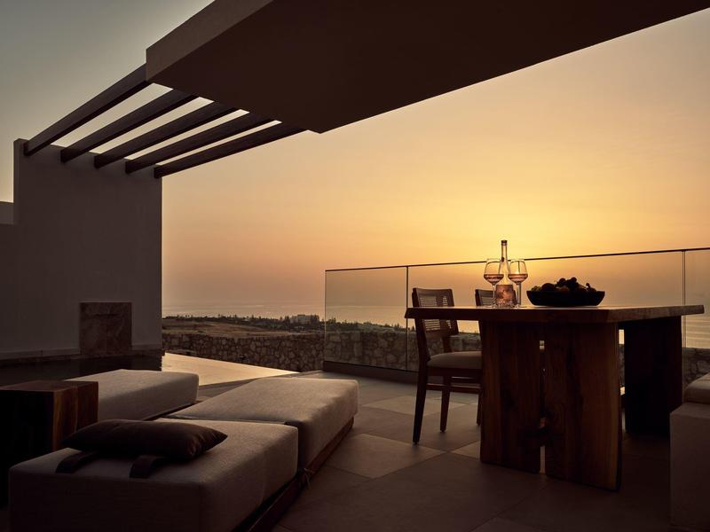 Sunset view from a modern terrace with lounge chairs and a wooden dining table.