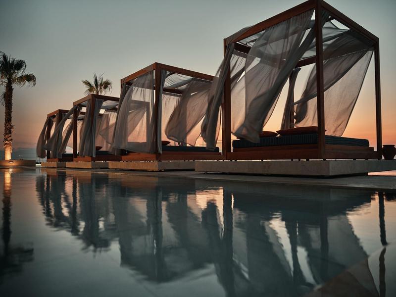 Sunset view of poolside cabanas with flowing curtains and palm trees at a luxury resort.