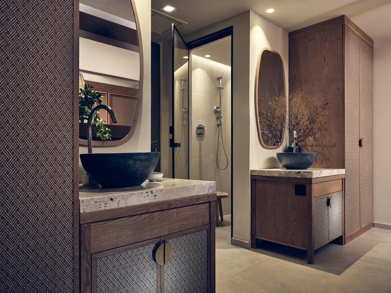 Modern hotel bathroom with elegant wooden vanities and oval mirrors beside a glass shower.