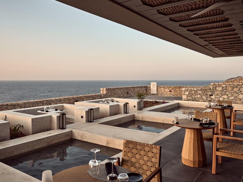 Sunset view from a hotel terrace with infinity pool overlooking the sea and rocky coastline.