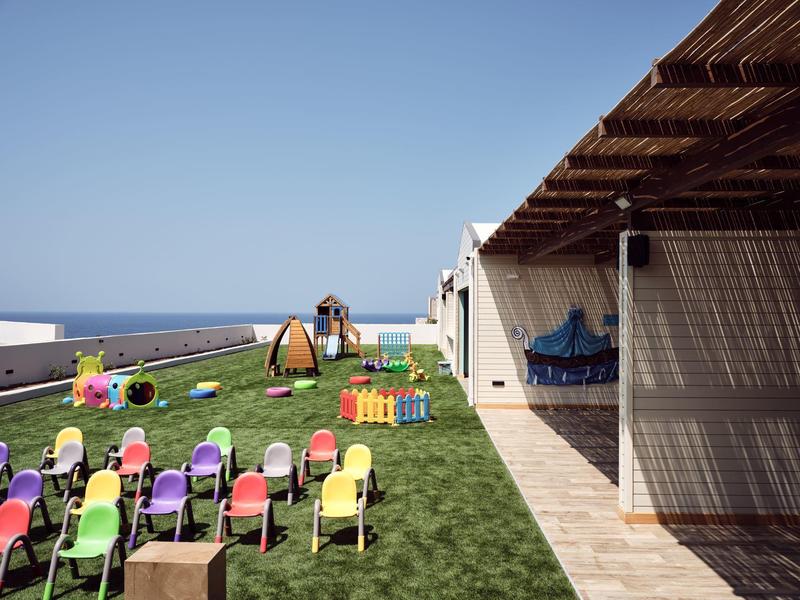 Outdoor seating and play area with colorful chairs and toys near a white building by the sea.