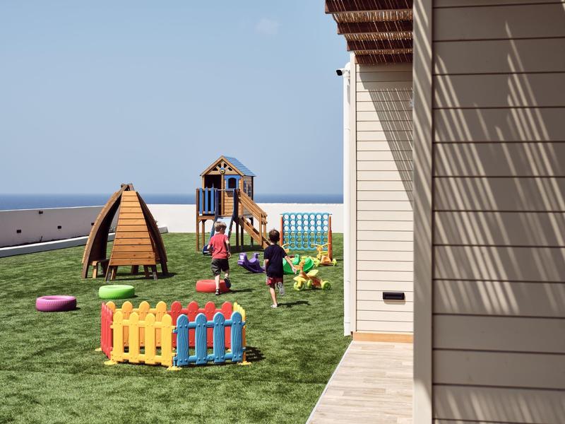 Outdoor playground with colorful play equipment and children by a building near the sea.