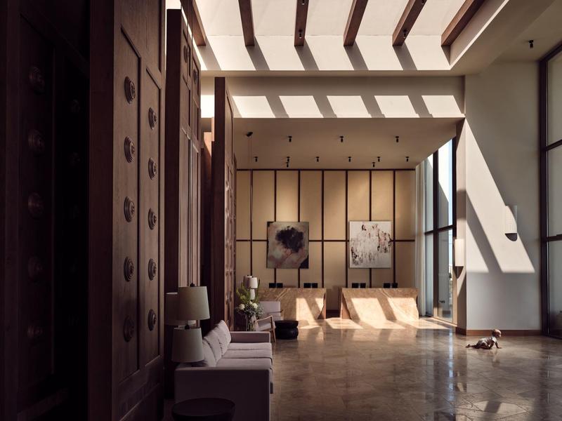 Hotel lobby with wooden panels, modern seating, and sunlight streaming through ceiling windows.