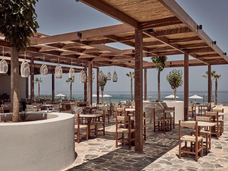 Outdoor wooden pergola with tables and chairs overlooking the sea under clear sky