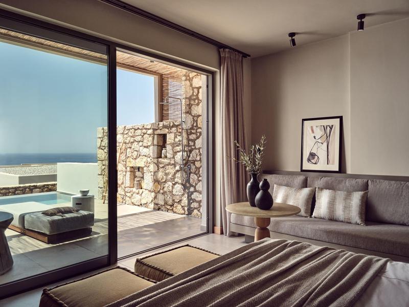 Modern hotel room with glass doors opening to a stone patio and ocean view.