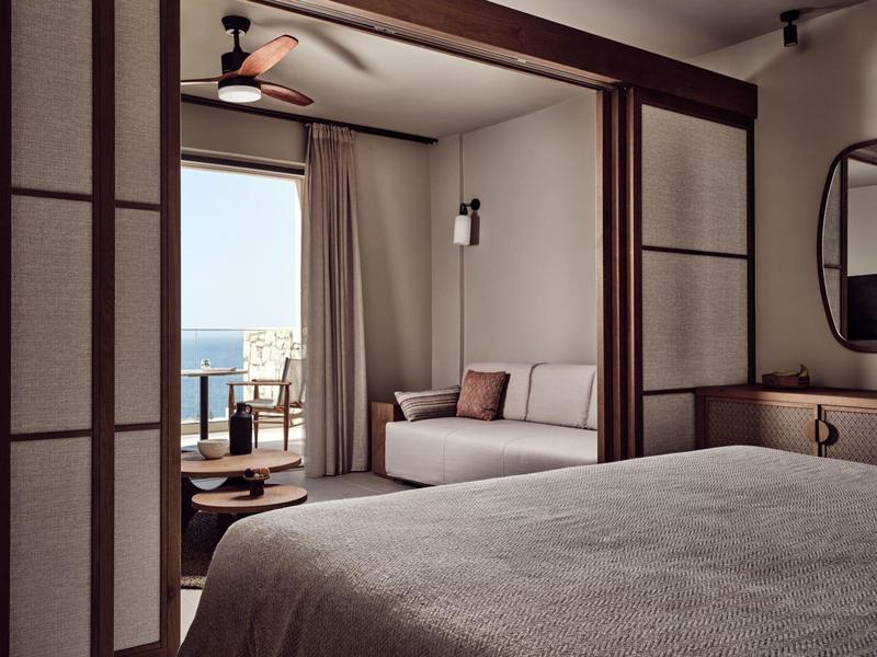Cozy hotel room with bed, seating area, and balcony overlooking the ocean.