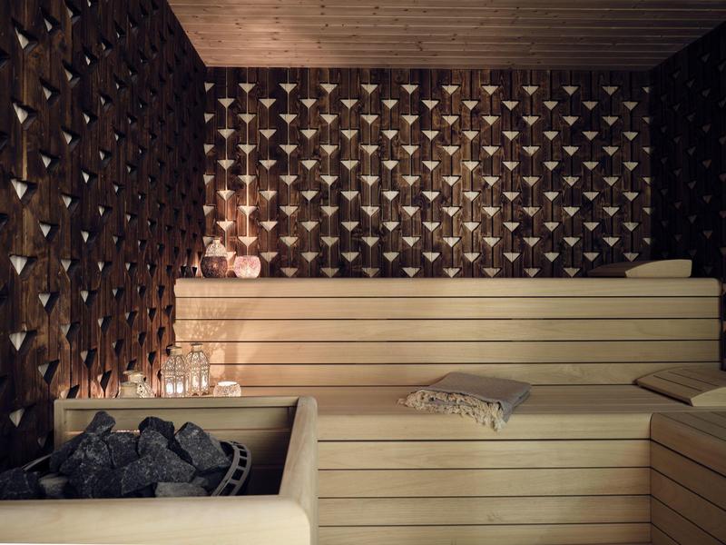 Cozy sauna with wooden benches, dark patterned walls, and lit candles creating warm light.