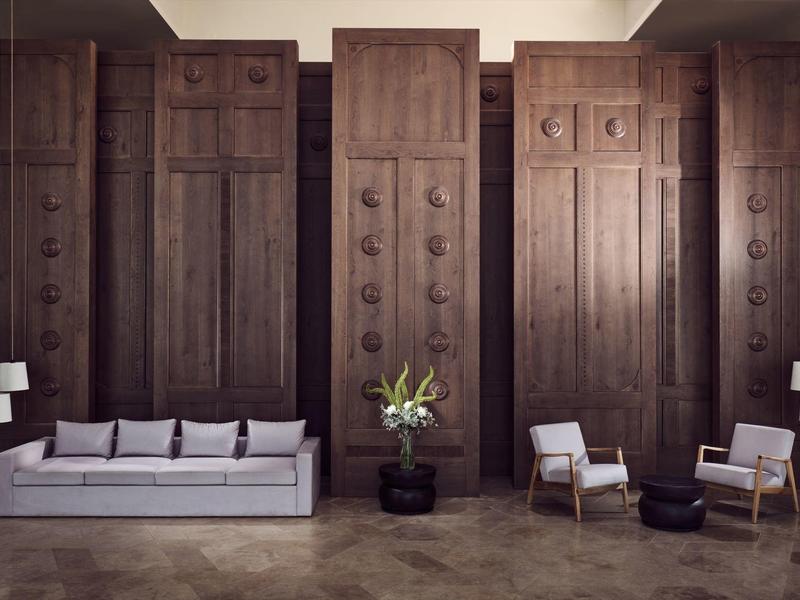 Modern lounge with wooden paneled walls, gray sofa, two armchairs, and floor lamps.