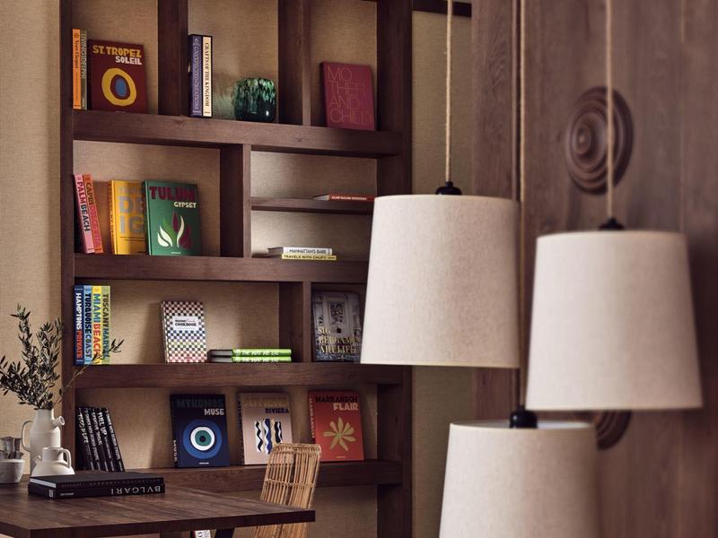 Cozy hotel lounge with wooden shelves, books, a desk, and three hanging white lamps.