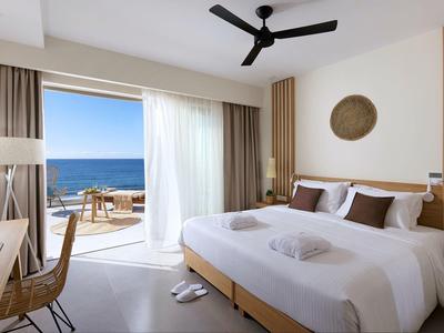 Moderner Hotelraum mit Doppelbett, Balkon und Blick aufs blaue Meer, helle Vorhänge und Holzdetails.