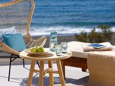 Terrasse mit Holzstuhl, Tisch, Apfelschale und Blick auf Meer bei klar blauem Himmel.